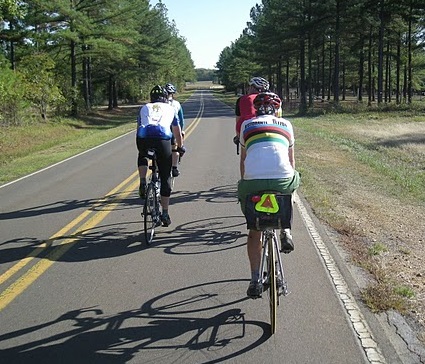 Cyclists riding double file on a narrow rural road. Riding double file deters unsafe same-lane passing in narrow lanes and makes the cyclists as visible as a car from the front and behind. [Mike Dayton photo]